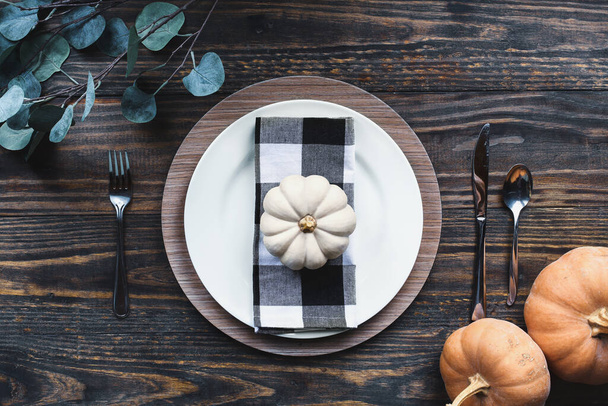 A Thanksgiving day holiday place setting with plate, napkin, on a decorated table shot from flat lay or top view position with orange and white pumpkins.  - Фото, изображение