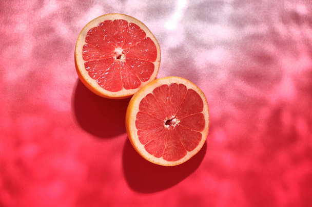 Fresh juicy grapefruit cut in half on a red background with the effect of water waves. Fresh summer fruits.  - Photo, Image