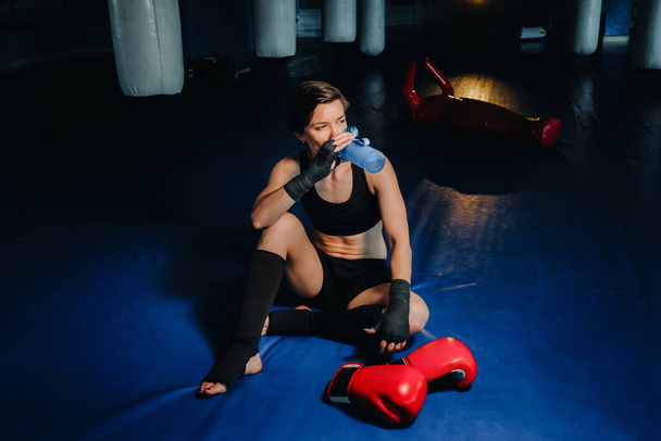 portrait of a female boxer in red gloves in the gym after a workout with a bottle of water. - 写真・画像