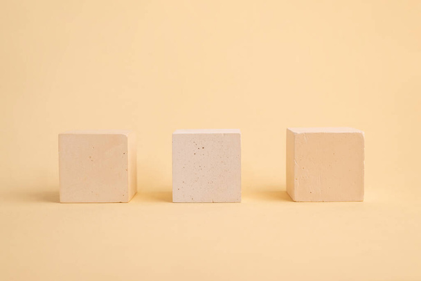 Drie concrete blokjes op een beige abstracte achtergrond. geometrisch podium. Lege vitrine voor de presentatie van cosmetische producten - Foto, afbeelding