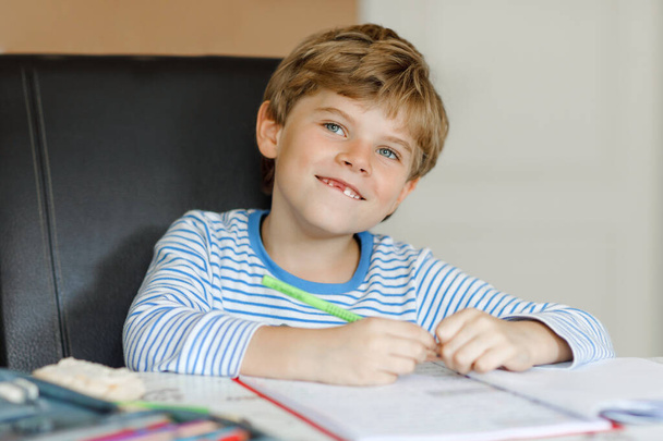 Retrato de lindo niño feliz escuela sana en casa haciendo tarea. Niño pequeño escribiendo con lápices de colores, en el interior. Escuela primaria y educación. Niño aprendiendo a escribir letras y números - Foto, Imagen