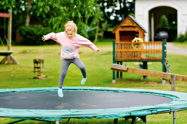 Küçük anaokulu kızı trambolinde zıplıyor. Mutlu küçük çocuk yazın açık hava aktiviteleriyle eğleniyor. Çocuklar için spor ve alıştırmalar. - Fotoğraf, Görsel