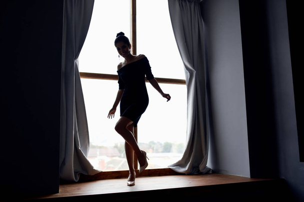mujer posando en vestido negro cerca de silueta de ventana modelo - Foto, Imagen