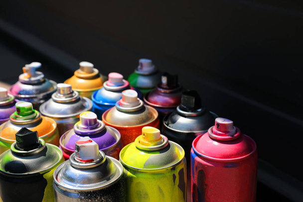 Used cans of spray paint on dark background, space for text. Graffiti supplies - 写真・画像