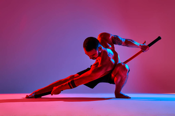 спортсмени силует з палицею тренування карате використовуючи спортивний інструмент в студії на кольоровому фоні вогнів
. - Фото, зображення