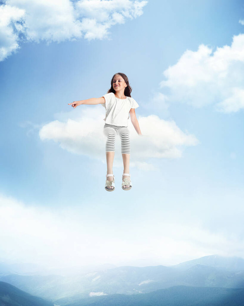 Creative artwork, collage with little beautiful girl sitting on white cloud and flying above forest, nature landscape. Concept of childhood, happiness, dreams - Фото, зображення
