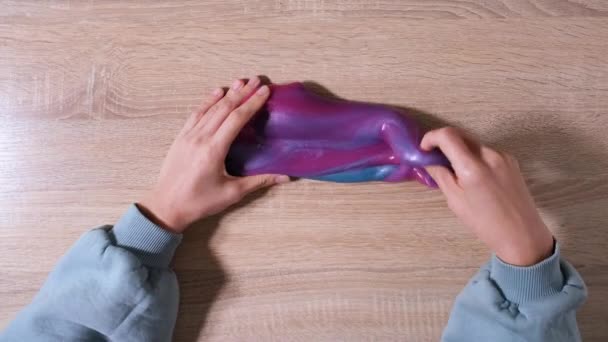 Spelen met slijm, rekken van de kleverige stof voor plezier en stress verlichting. Close-up en bovenaanzicht van vrouwelijke hand die blauw, roze en paars glanzend slijm vasthoudt en knijpt. 4K-video - Video