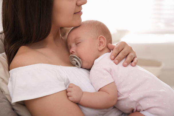 Happy young mother with her sleeping baby on chair  at home, closeup - Foto, imagen