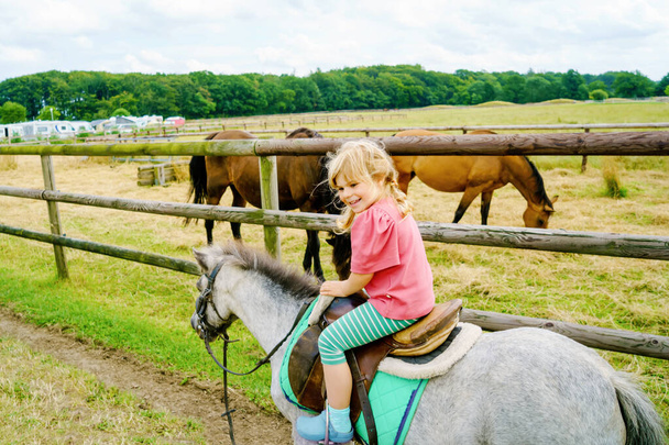 Kleine Vorschulmädchen reiten auf einem Pony auf einem Bauernhof. Glückliches schönes Kind, das Reiten übt. Sommeraktivitäten im Freien für Kinder. Beliebte Sportart für kleine Mädchen. - Foto, Bild