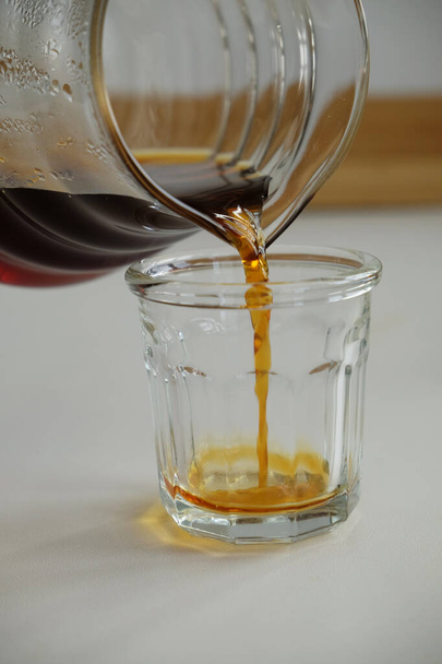Specjalna koncepcja kawy. Czarny filtr kawy wlewa się do szklanej filiżanki z dekantera szklanego zbliżenie - Zdjęcie, obraz