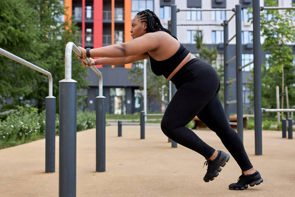 Beautiful african overweight young woman does fitness outdoors. Fat lady is training - Fotografie, Obrázek