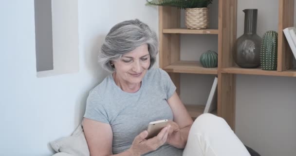 Donna anziana sorpresa dai contenuti online, guarda lo schermo del suo smartphone e guarda un'istantanea o un video umoristico. - Filmati, video