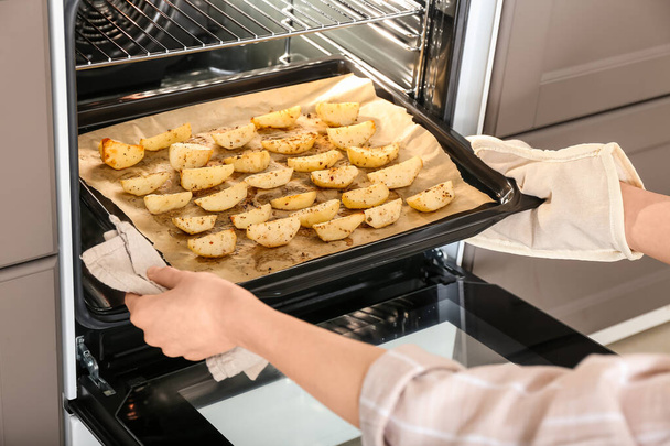 Frau holt Backblech mit frischen Kartoffeln aus dem Ofen - Foto, Bild