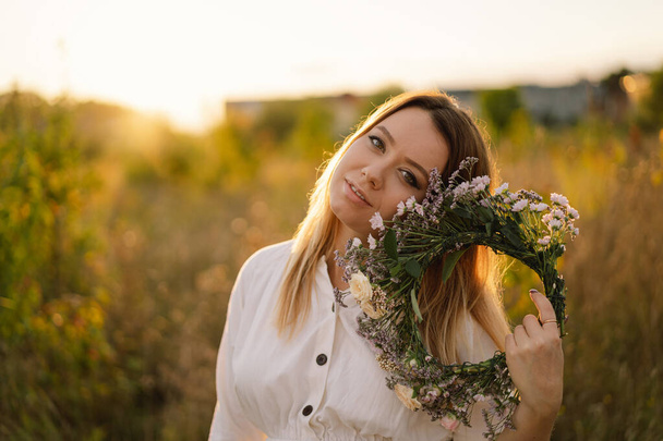 Vahşi çiçeklerden bir çelenk içinde güzel bir genç kadının yaz hayat portresi. Kafasında çelenk var. - Fotoğraf, Görsel