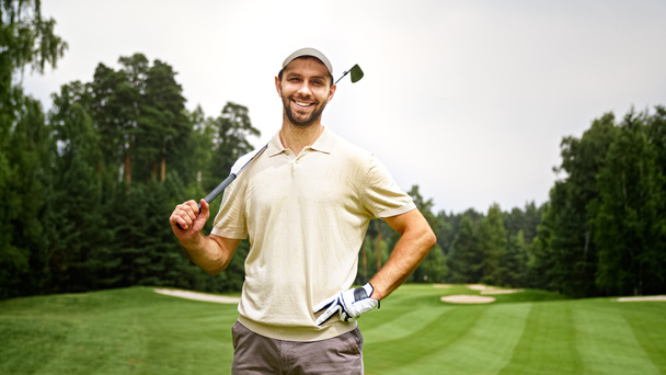 Młody człowiek z kijem golfowym patrzący w kamerę na polu golfowym - Zdjęcie, obraz
