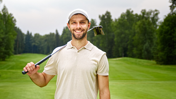 Young man with golf club looking at camera at golf course outdoors - Photo, Image