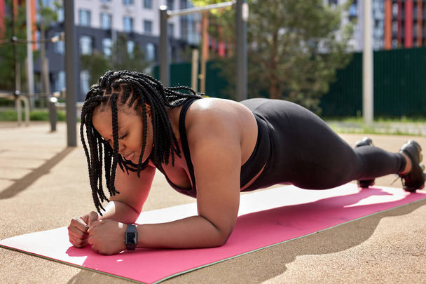 Strong fat female doing plank on fitness mat outdoors, side view portrait, focused - Fotoğraf, Görsel