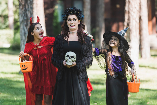 girls in devil and witch halloween costumes frightening scared mom in forest - Photo, Image