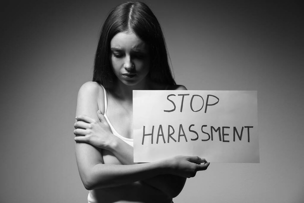 Junge Frau hält Papier mit dem Text STOP HARASSMENT auf grauem Hintergrund - Foto, Bild