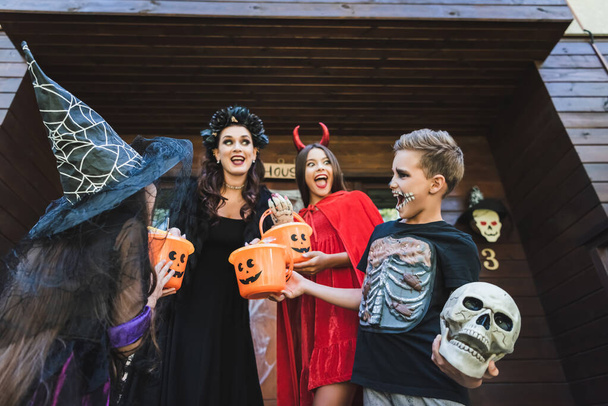 Niedrigwinkel-Ansicht der aufgeregten Familie in gruseligen Halloween-Kostümen schreit auf der Veranda der Hütte - Foto, Bild