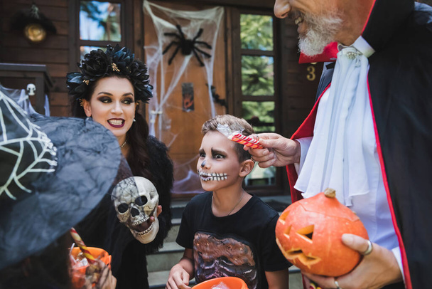 чоловік тримає цукерки поблизу збудженої сім'ї в костюмах Хеллоуїна
 - Фото, зображення
