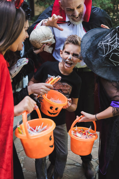 familie in halloween kostuums grimmig terwijl het houden van emmers met snoep - Foto, afbeelding