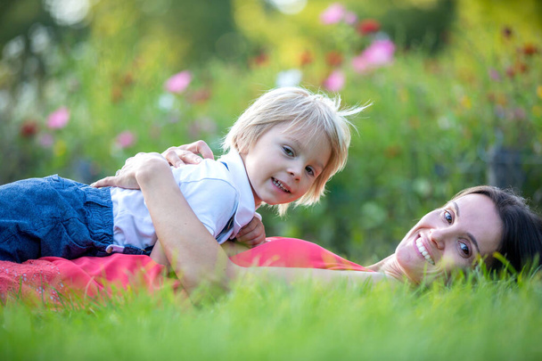 Mother and cute blond child, boy, lying in the grass, hugging and enjoying a tender moment between each other - 写真・画像