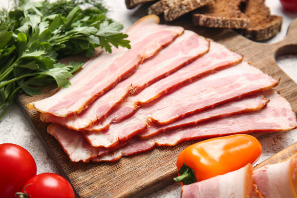 Wooden board with slices of tasty smoked bacon and fresh vegetables on light background - Fotoğraf, Görsel
