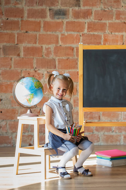 Portrait of caucasian school kindergarten girl standing in front of blackboard with pencils in her hands, back to school concept - Foto, afbeelding