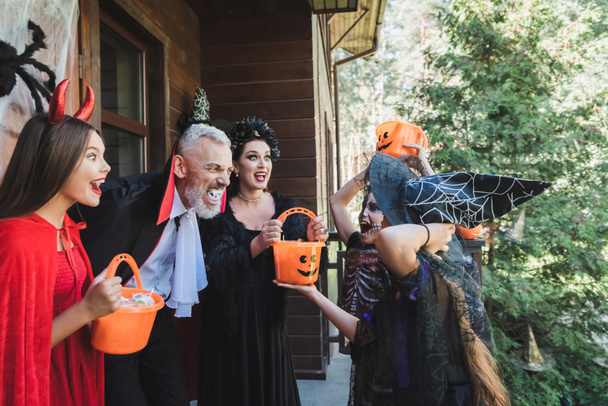 excited couple in spooky halloween costumes scaring kids near house - Fotografie, Obrázek
