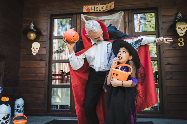 чоловік у вампірському костюмі лякає дочку біля будинку з прикрасою Хеллоуїна
 - Фото, зображення