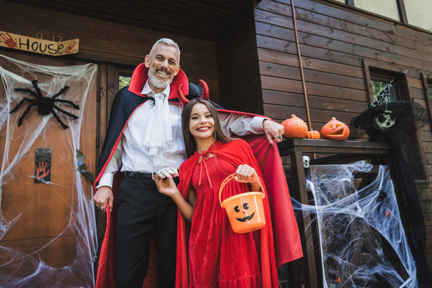 happy father and daughter in halloween costumes near cottage with decoration - Foto, Imagen