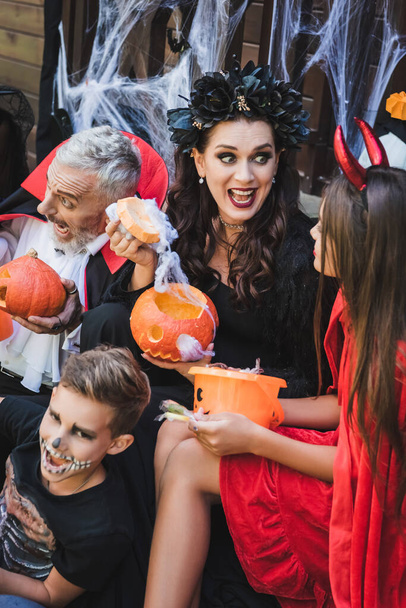 Aufgeregte Frau mit geschnitztem Kürbis bei Familie in Halloween-Kostümen - Foto, Bild