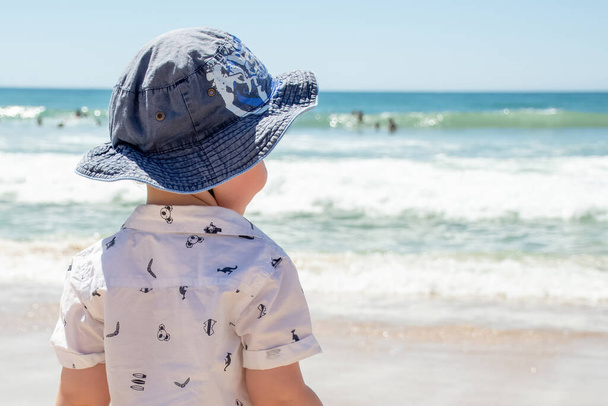 Un ragazzino che indossa un cappello su una spiaggia sabbiosa dell'oceano in Australia. Protezione solare - Protezione solare, cappello e camicia. Viaggiare con i bambini. - Foto, immagini