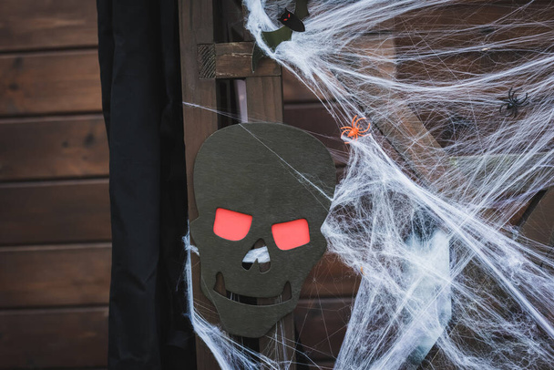 spider net with toy spiders near spooky paper cut skull on wooden fence - Foto, Bild