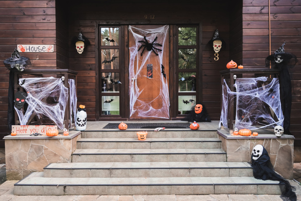 Eingang der Hütte mit geschnitzten Kürbissen, Spinnennetz, Spielzeugspinnen und Fledermäusen aus Papier dekoriert - Foto, Bild