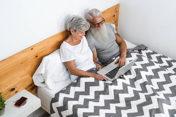 Happy vanhempi pari hauskaa katsomassa tietokonetta makaamassa sängyssä alla huopia - Teknologia ja vanhusten elämäntapa käsite - Valokuva, kuva