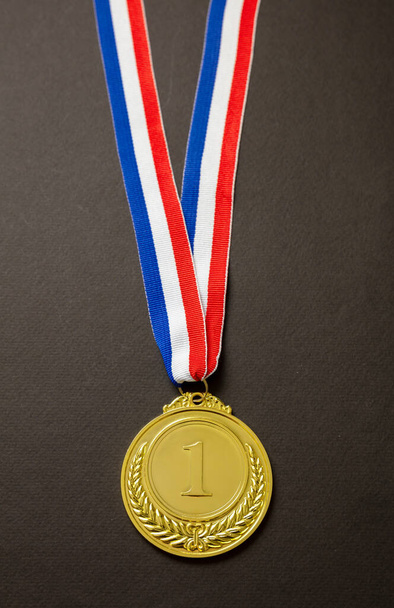 Złoty Medal, Nagroda Zwycięzcy wisząca na czerwonej niebieskiej wstążce. Trofeum sportowca w sporcie dla pierwszego miejsca mistrz izolowany na czarnym tle. - Zdjęcie, obraz
