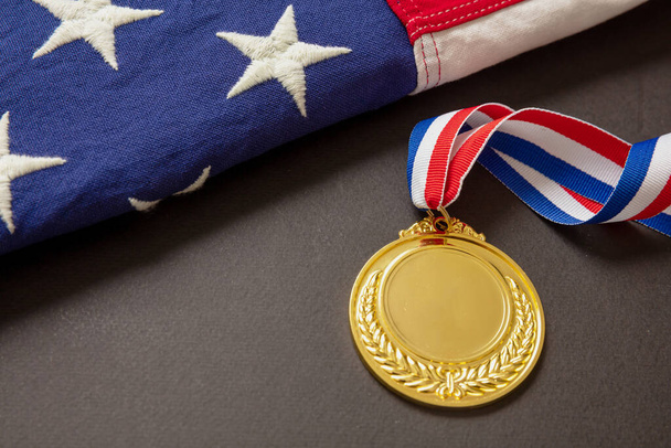 Medal gold for USA. Winner prize award with ribbon and US flag on black background. American athlete trophy in sport for first place champion. Blank space and laurel wreath, template - 写真・画像