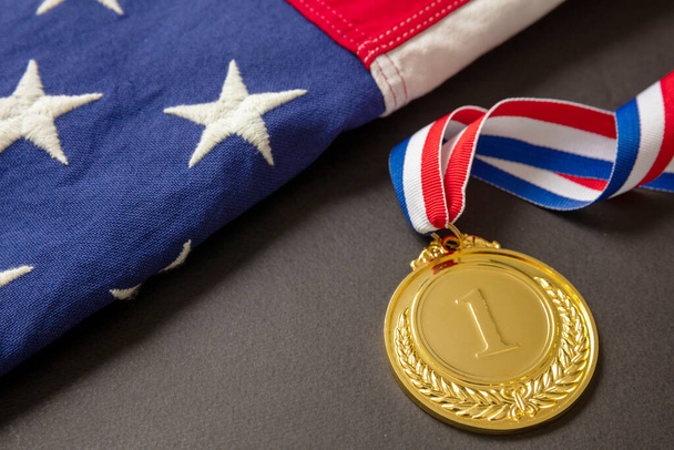 Χρυσό μετάλλιο για τις ΗΠΑ. Βραβείο νικητή με κορδέλα και αμερικανική σημαία σε μαύρο φόντο. American αθλητής τρόπαιο στον αθλητισμό για την πρώτη θέση πρωταθλητής. - Φωτογραφία, εικόνα