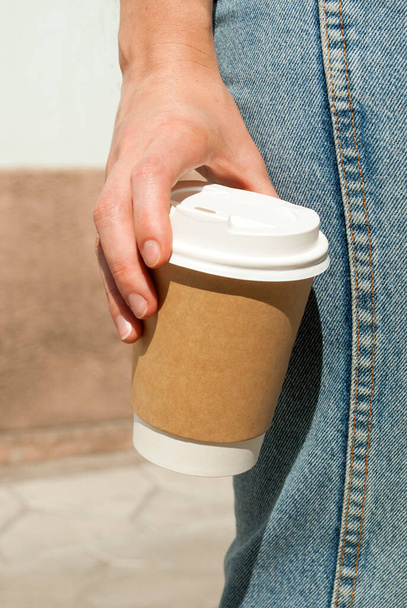 Woman, coffee, city.Big paper cup for cappuccino or latte in a woman's hand on a background of jeans. Coffee to go. Empty space for text, mock up  - Fotó, kép