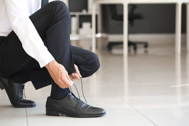Businessman tying shoe laces in office - 写真・画像