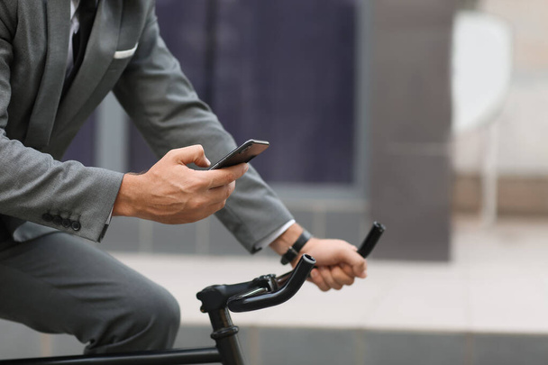 Businessman with mobile phone riding bicycle on city street - Foto, Imagem