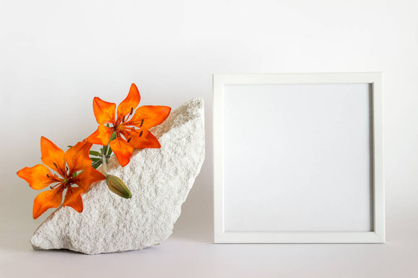 Mockup template with square white wooden frame, porous white stone and orange lilies on whiote background. - Foto, imagen