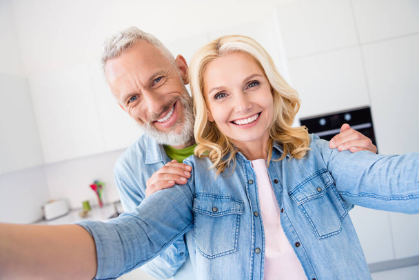 Photo of pretty sweet aged couple wear denim shirt smiling making self photo indoors house room - Zdjęcie, obraz