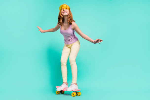 Фотографія повного розміру смішної блондинки дівчина-підліток йде скейт носити шапочку зверху штани ізольовані на кольоровому фоні
 - Фото, зображення