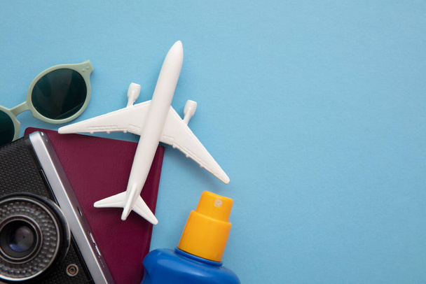 Overhead view of essential holiday travel items with a toy airplane on a blue background - Foto, Bild