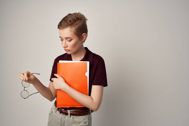 female student with an orange folder in hand light background - Photo, Image
