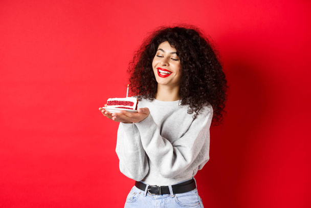 Happy Birthday Mädchen feiert und macht Wünsche, hält Kuchen und lächelt, steht auf rotem Hintergrund - Foto, Bild