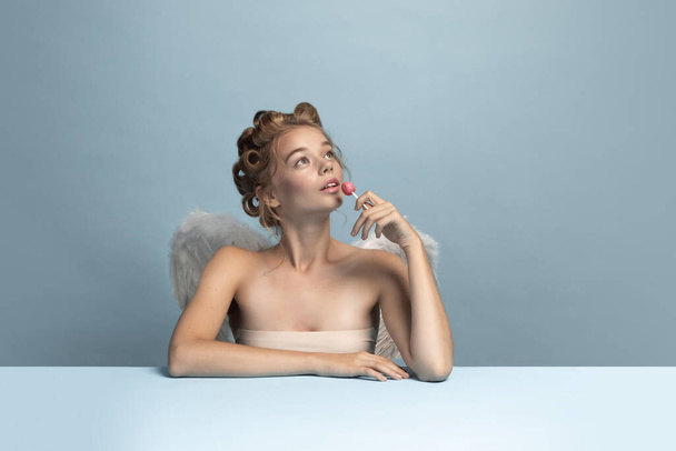 Dreaming angel, young beautiful girl sitting and thinking about cute moments of life isolated on blue gray studio background. Concept of beauty, purity, tenderness - Foto, afbeelding
